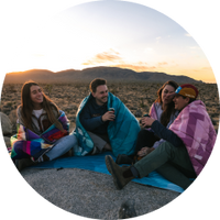 Four friends on a trip at Joshua Tree National Park, huddled up on an Everywhere Mat and keeping warm with Rumpl Original Puffy Blankets.