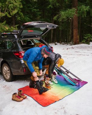 Two people sitting at the back of a car putting on ski gear