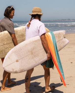 Two people walking on a beach with surfboards and towels