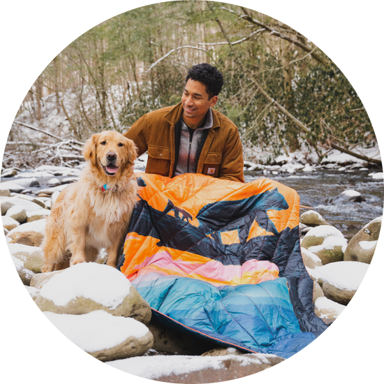  A man with a dog sitting on the snow with the Original Puffy Blanket - Great Smoky National Park blanket