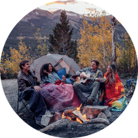 Four friends gathered around a campfire with Rumpl blankets, having a great time.